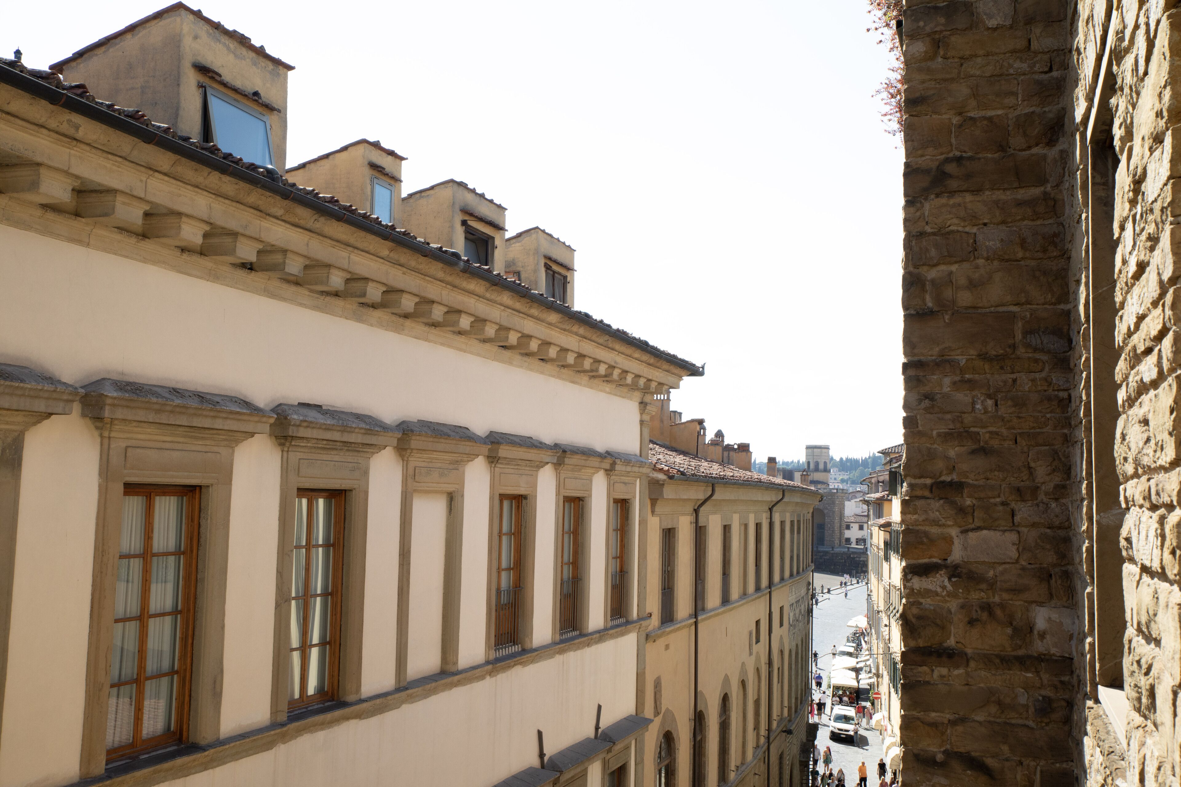 A narrow street flanked by historic buildings with arched windows and a stone wall on one side.