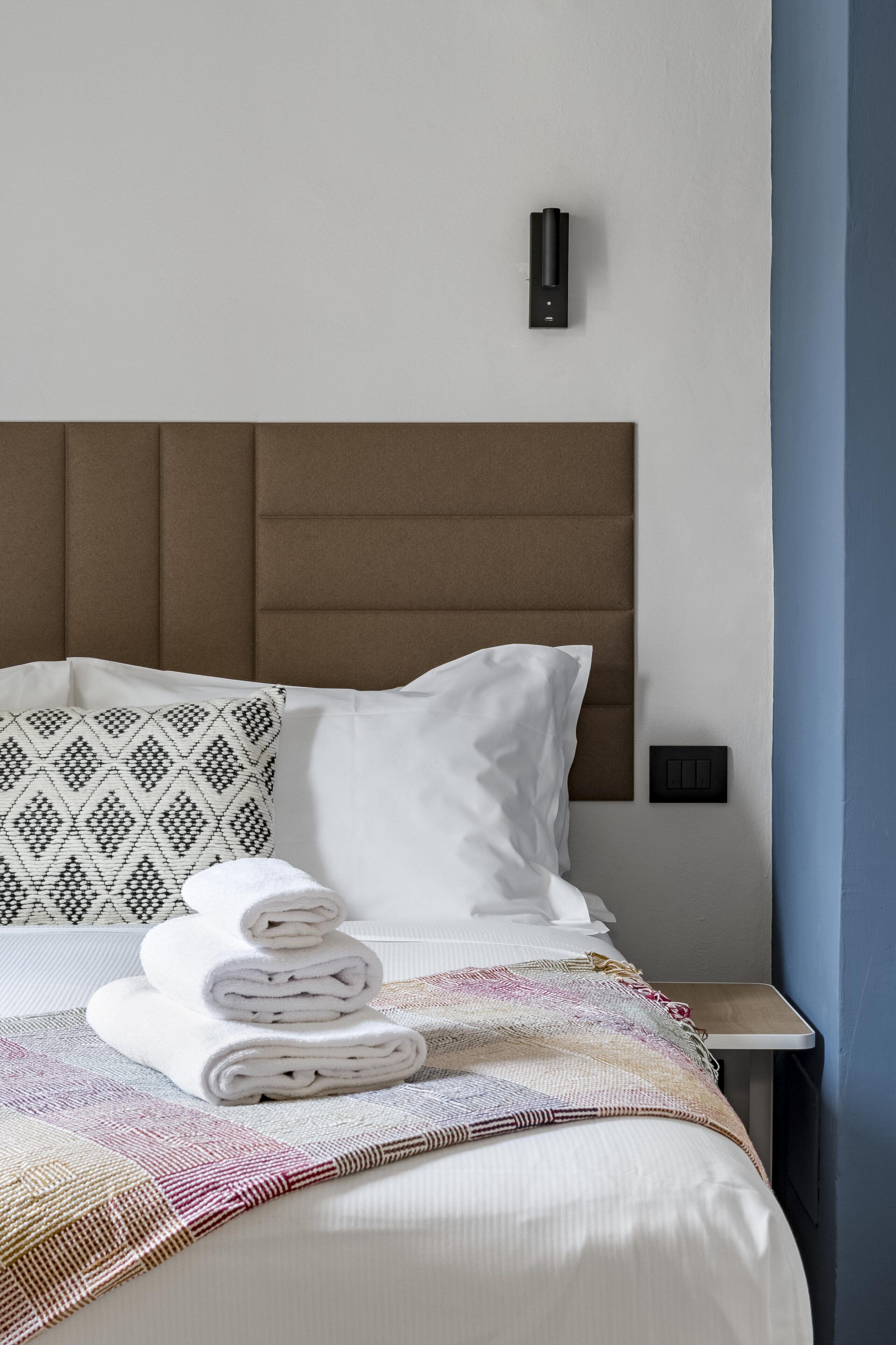 A neatly made bed with a patterned pillow, a folded white towel, and a woven blanket.