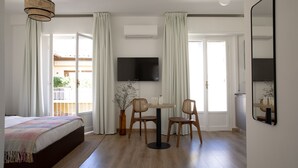 Een slaapkamer met een bed, een televisie, een tafel met stoelen en een raam met gordijnen.