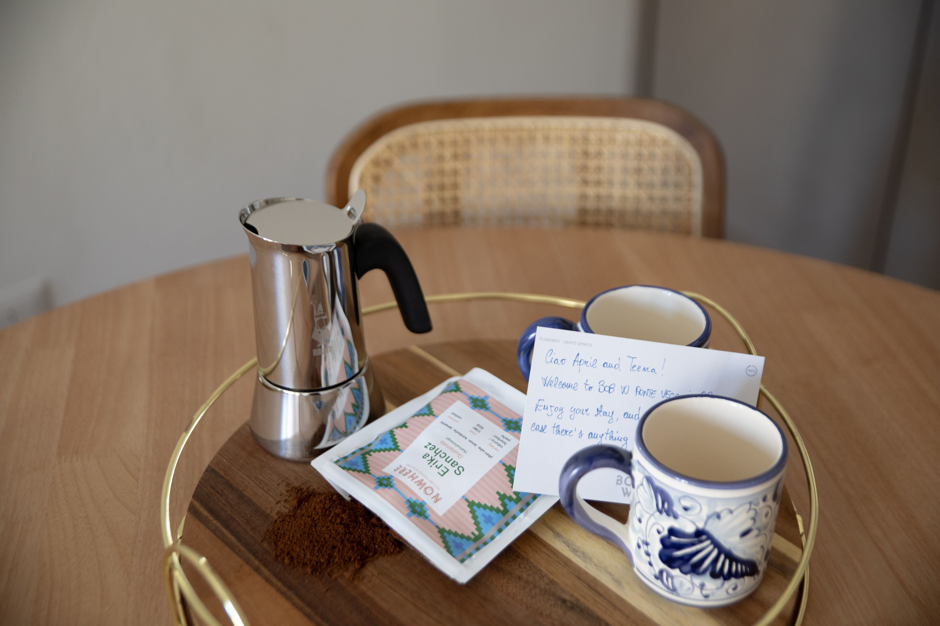 Uma bandeja com um coador de café, um cartão e uma caneca em uma mesa de madeira.