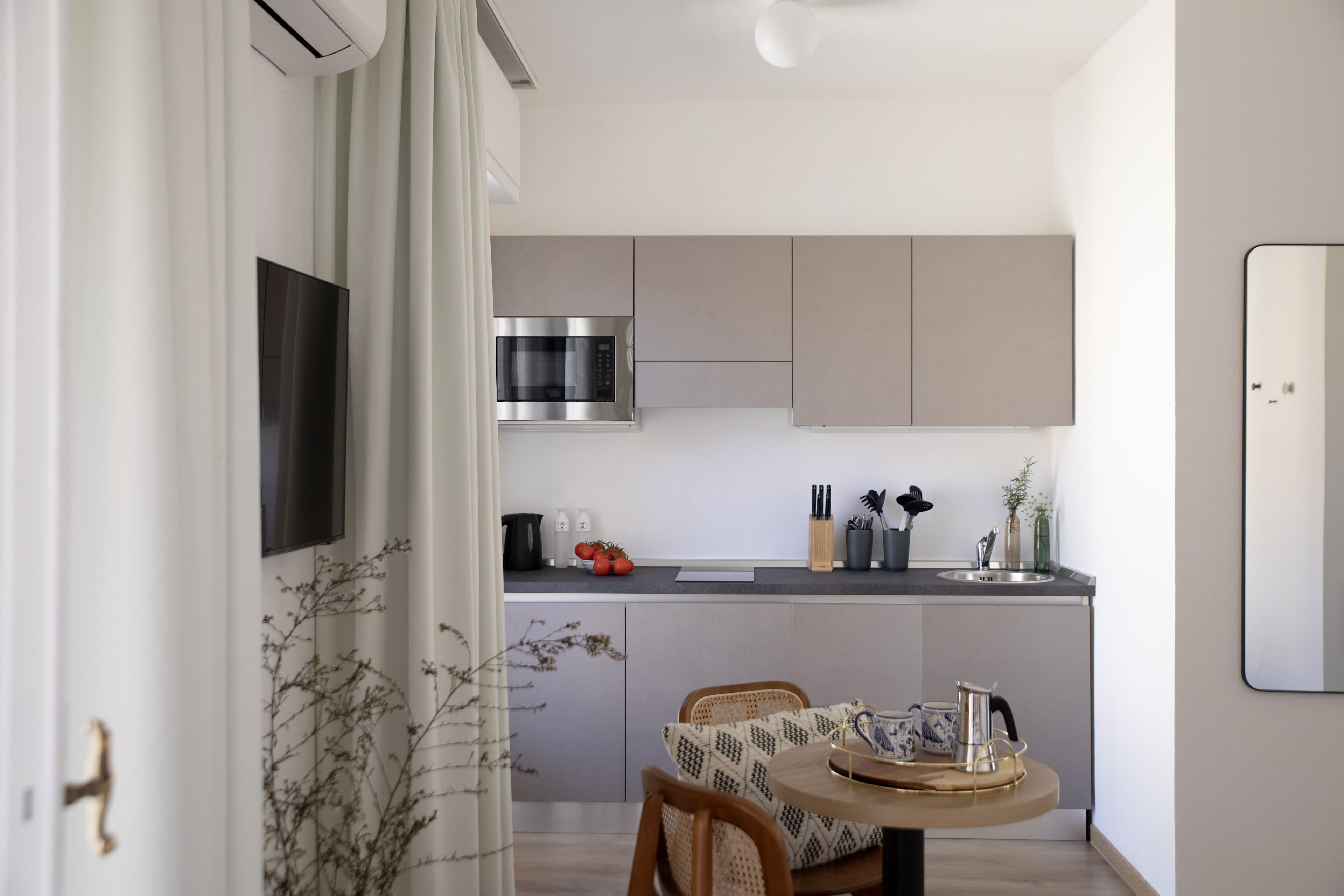 A modern kitchen with grey cabinets, a stainless steel microwave, and a sink. There is a dining area with a round table and chairs.