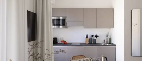 A modern kitchen with grey cabinets, a stainless steel microwave, and a sink. There is a dining area with a round table and chairs.