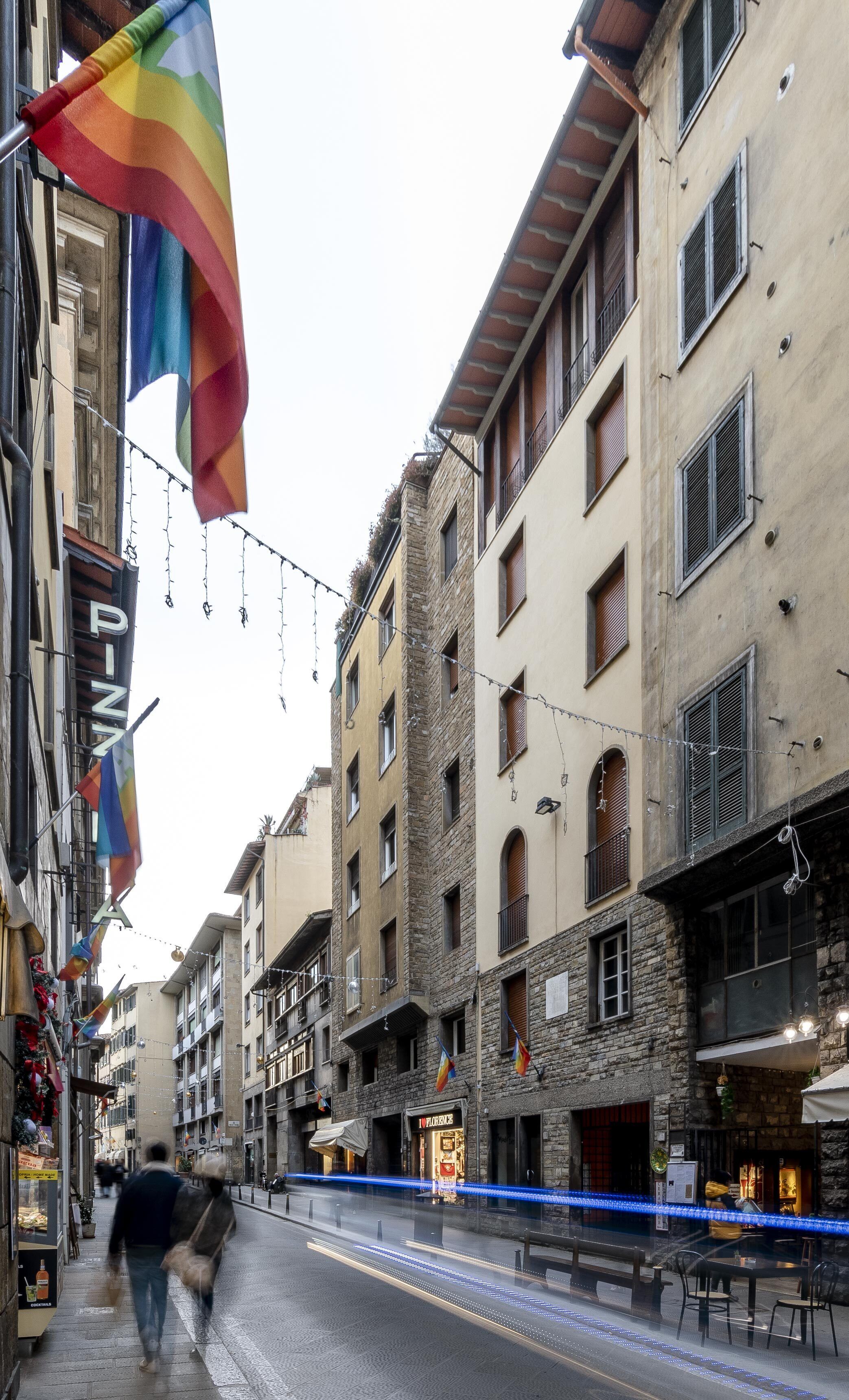 A street with buildings, a rainbow flag, and a sign for 'PIZZA'.