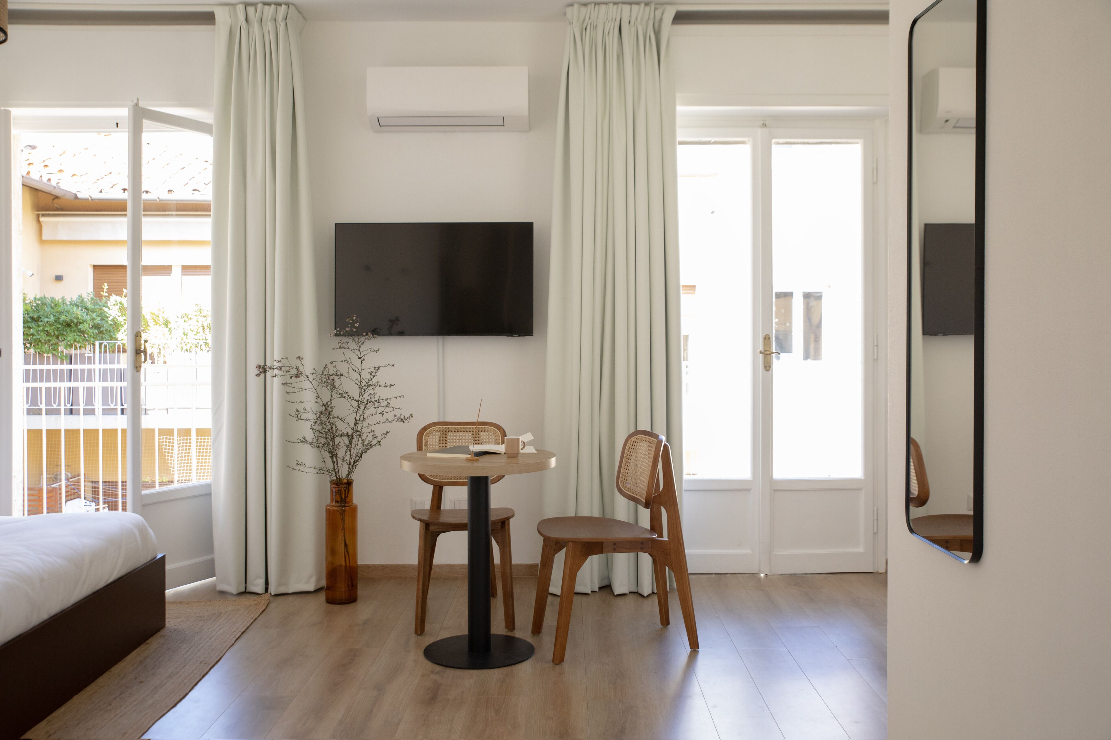 Une chambre à coucher avec un lit, un téléviseur fixé au mur et un coin repas comprenant une table et des chaises.
