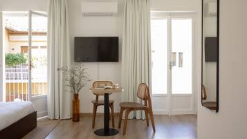 Une chambre à coucher avec un lit, un téléviseur fixé au mur et un coin repas comprenant une table et des chaises.