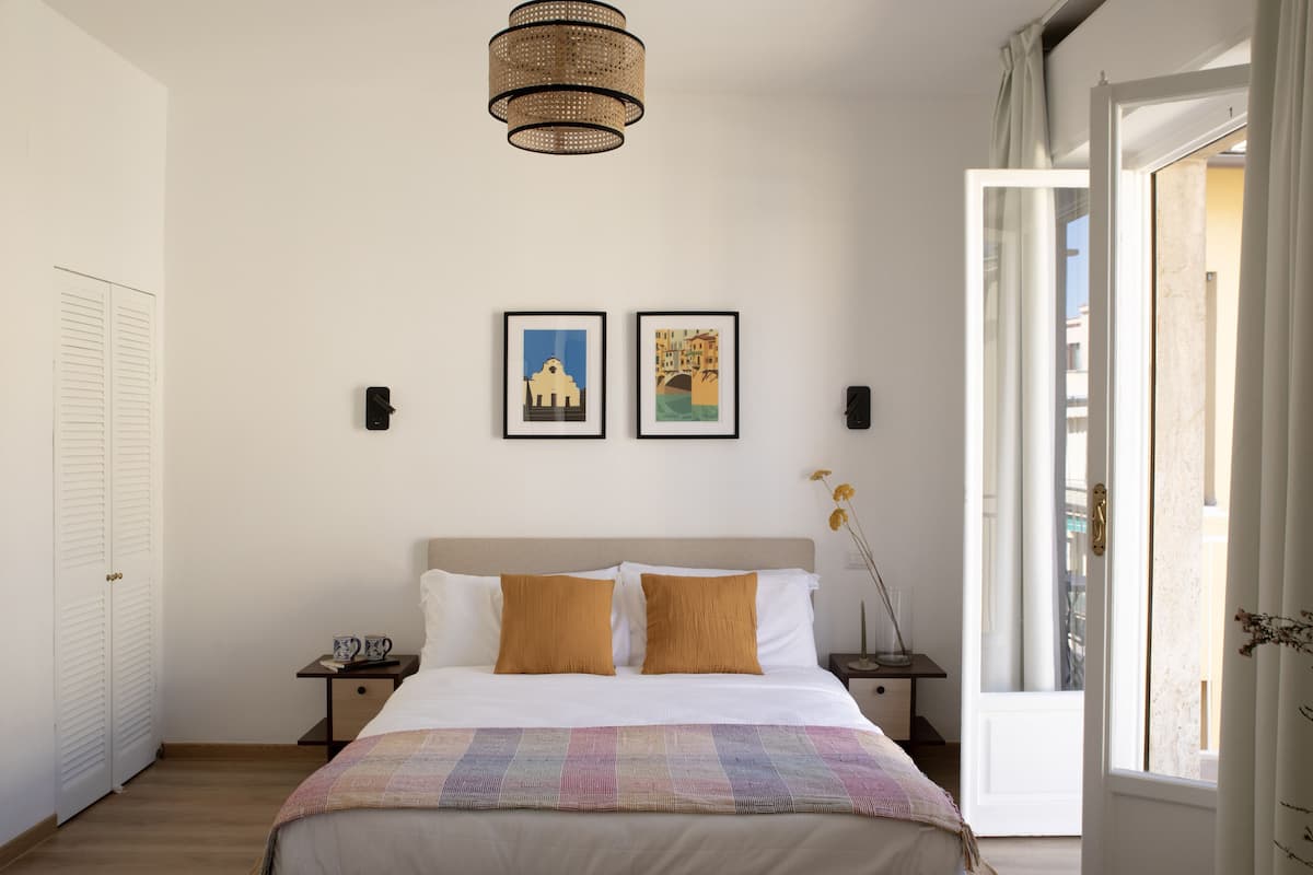 A bedroom with a bed, two bedside tables, a hanging light fixture, and two framed pictures on the wall.