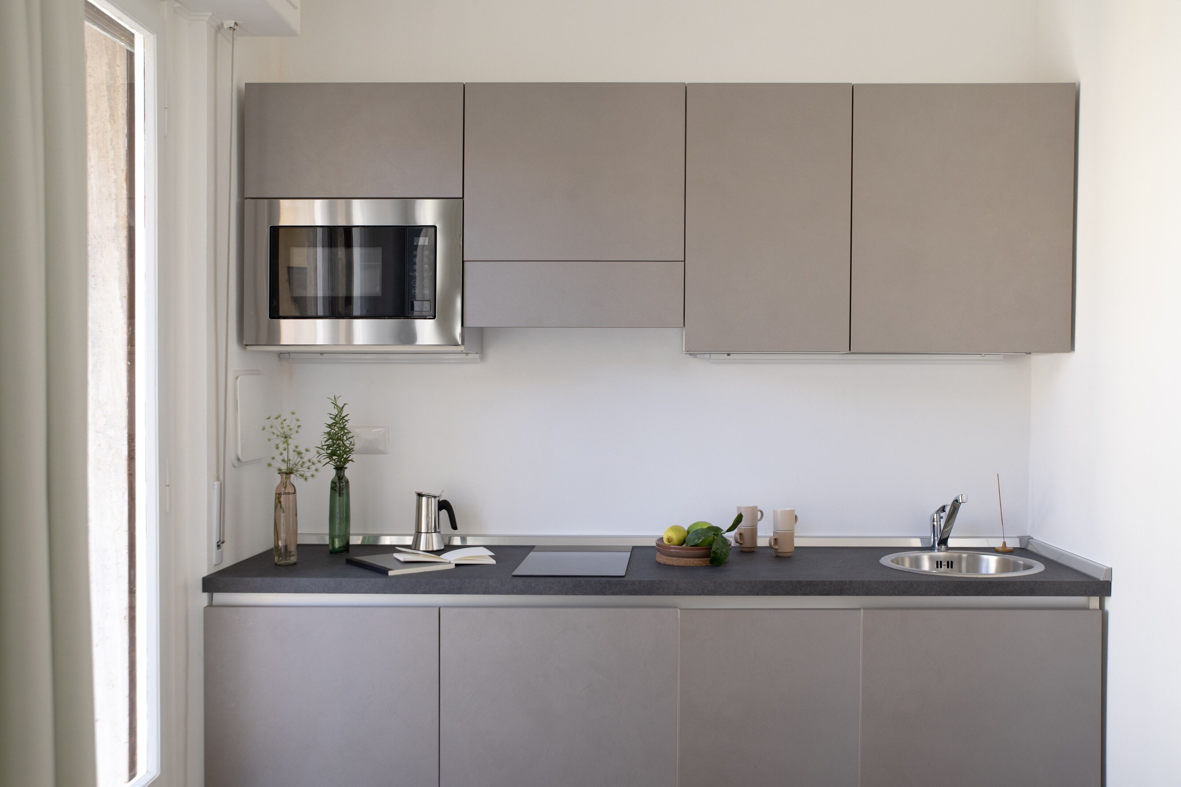 A modern kitchen with a stainless steel microwave, a sink, and a window providing natural light.