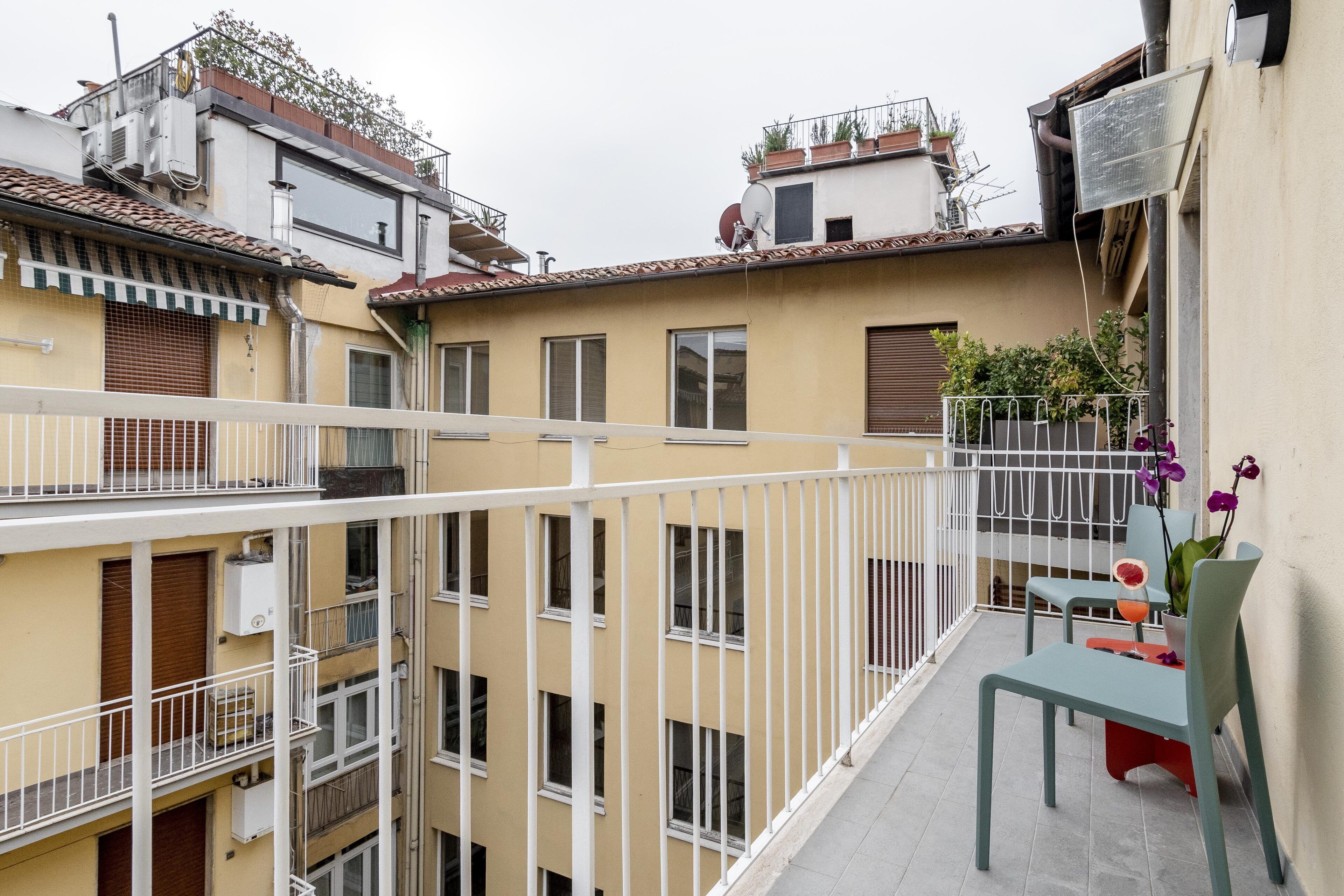 Un immeuble à plusieurs étages doté de balcons, d’une terrasse avec une table et des chaises, et de plantes en pot.