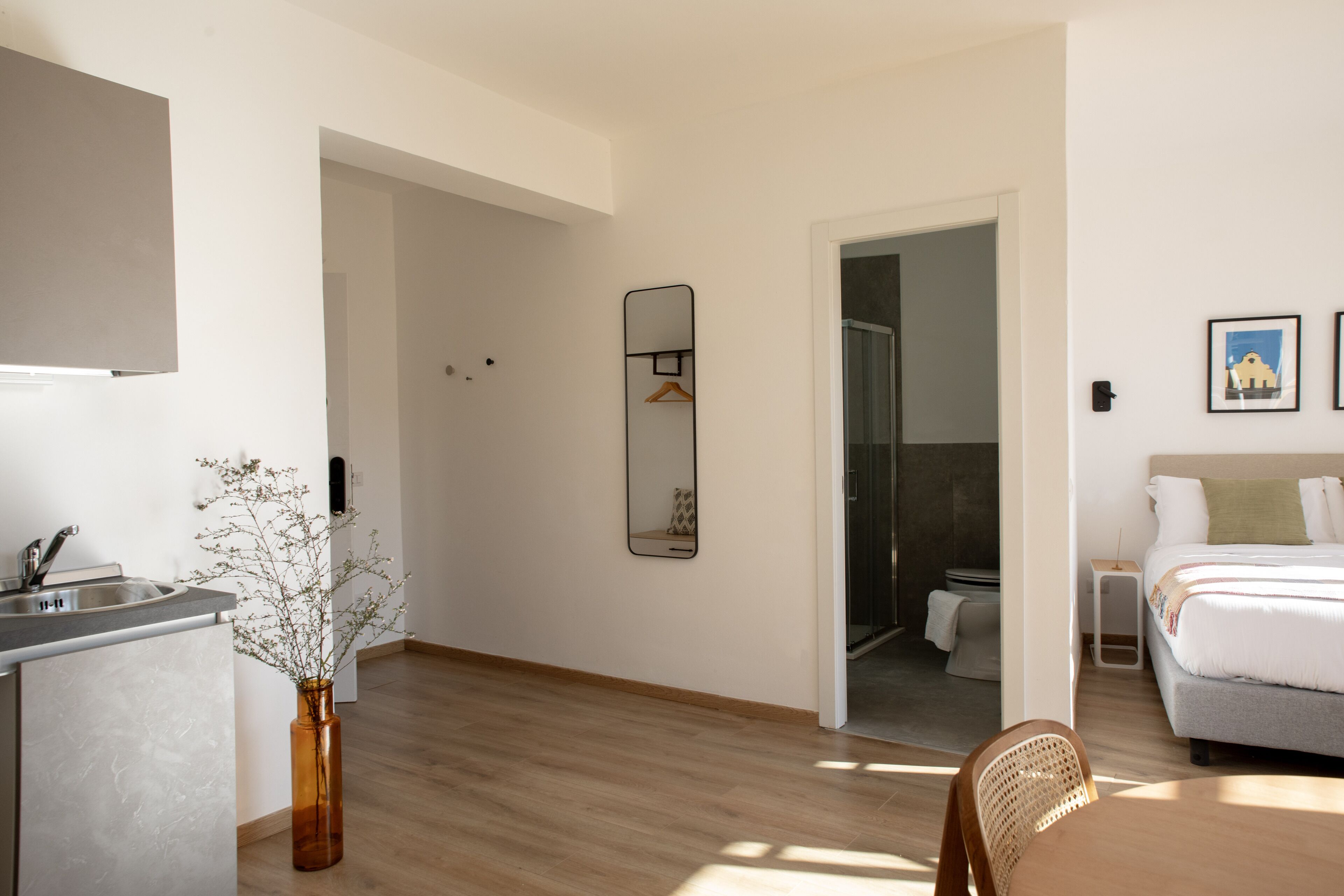 Een moderne hotelkamer met een kitchenette, een grote spiegel, een bed en een zithoek.