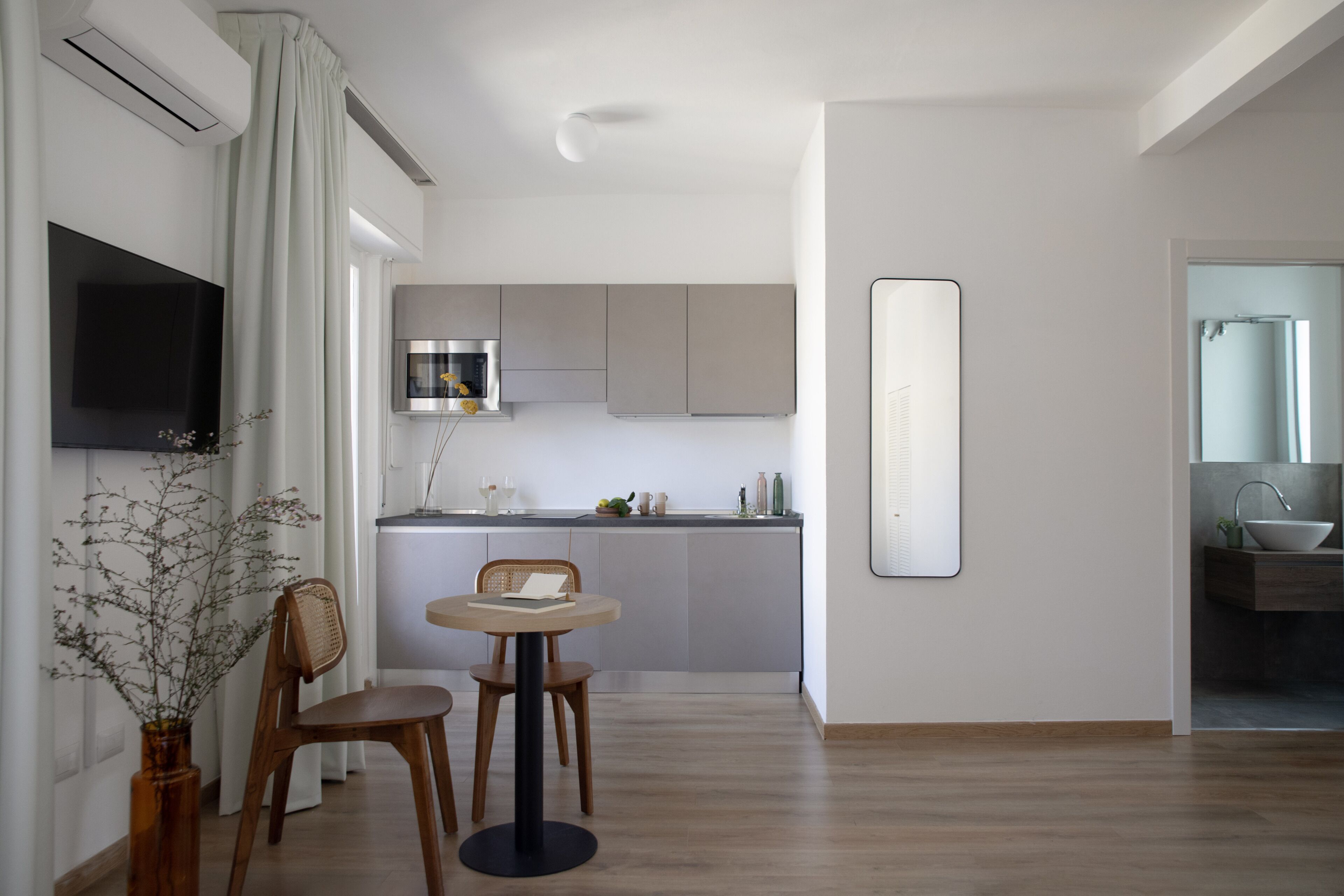 A modern kitchen with a flat-screen TV, a dining area with a round table and chairs, and a large mirror on the wall.