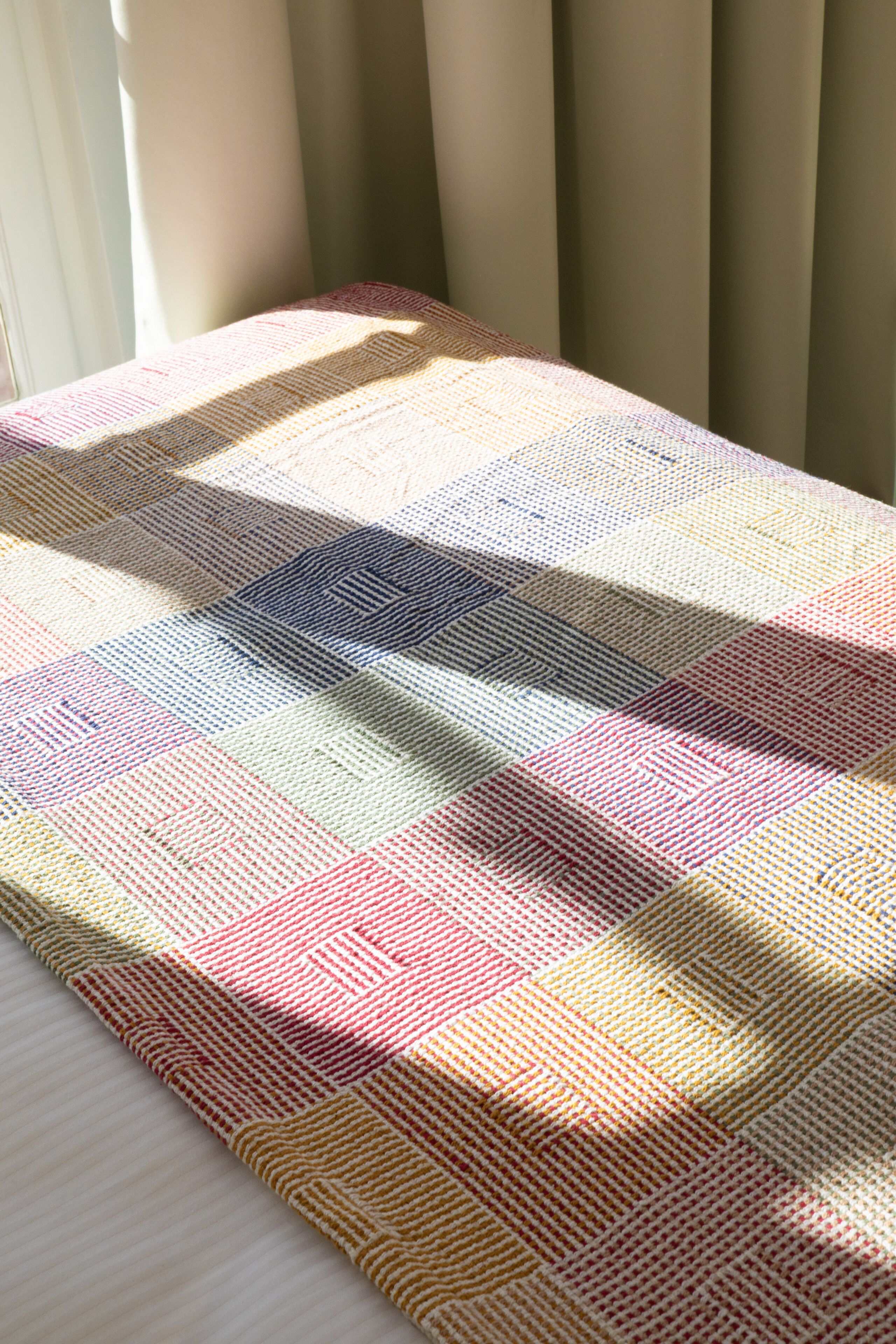 A checkered blanket on a bed with a window and curtains in the background.
