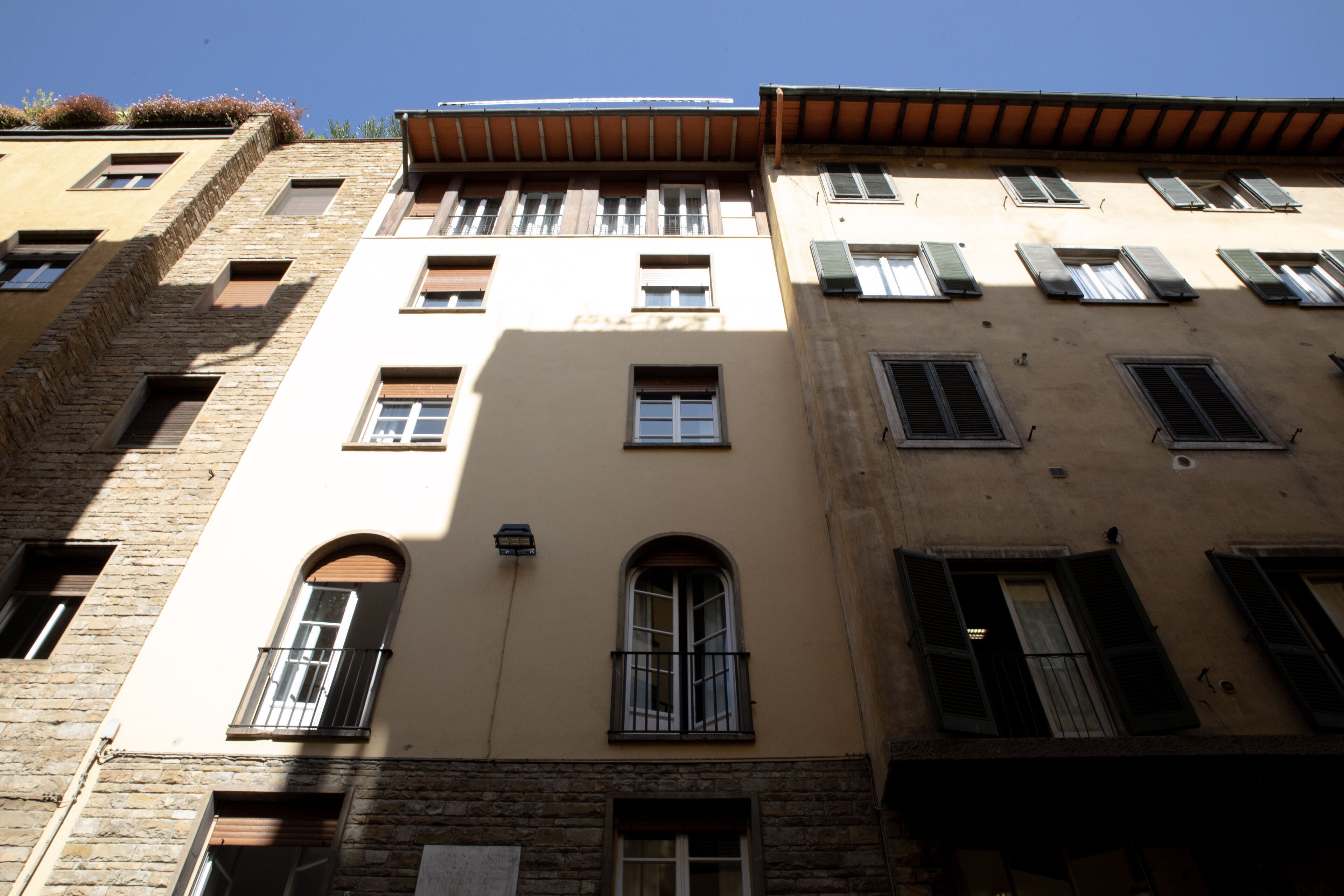Ein mehrgeschossiges Gebäude mit einer Fassade aus Backstein und Putz, zahlreichen Fenstern mit Fensterläden und einem Flachdach.