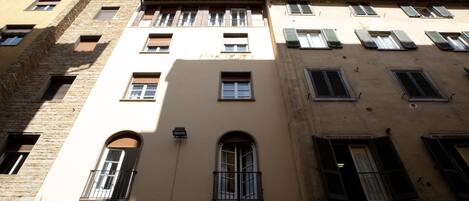 A multi-story building with a mix of brick and plaster facades, multiple windows with shutters, and a flat roof.
