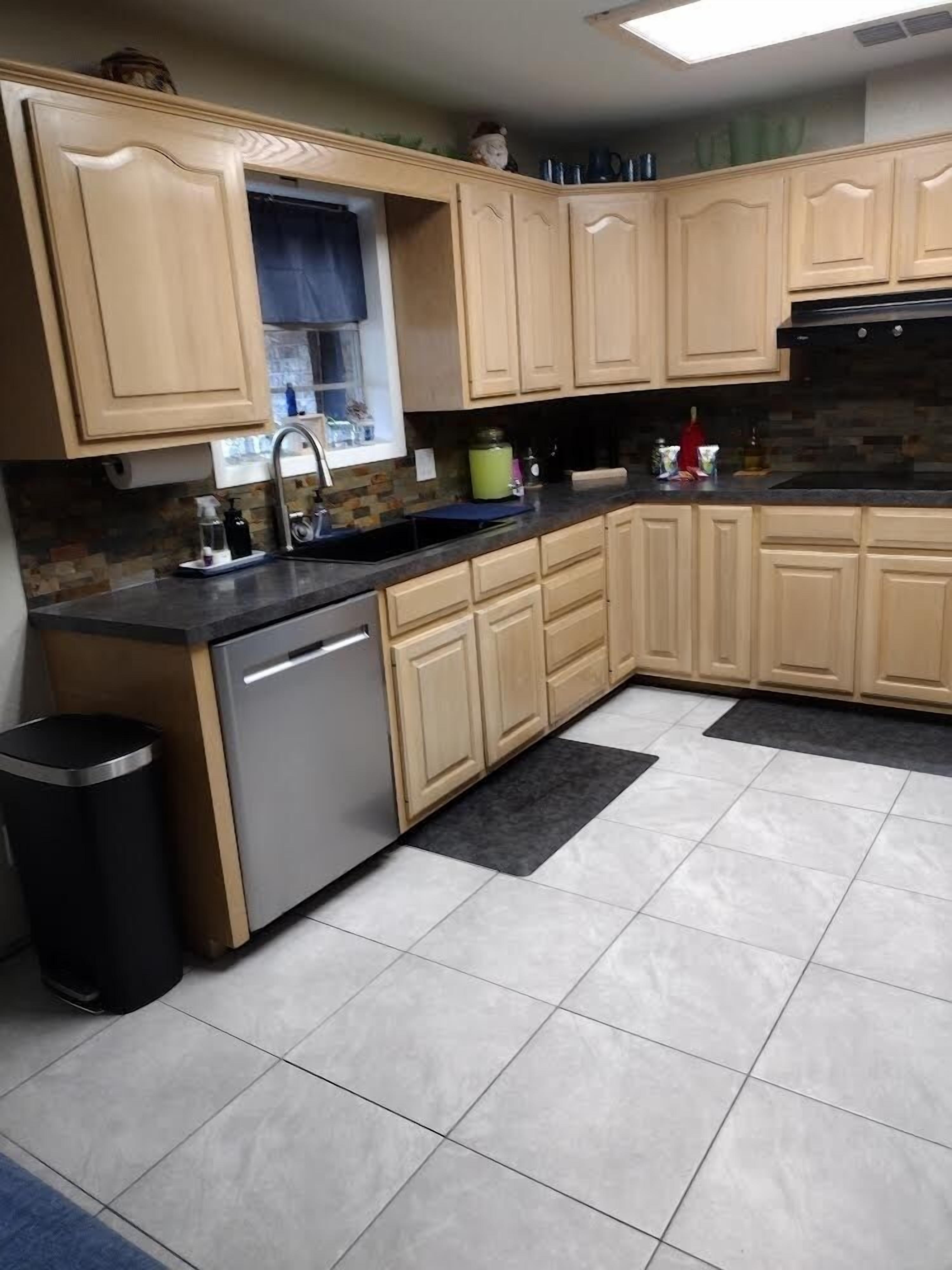 Una cocina con armarios de madera clara, lavavajillas de acero inoxidable y piso de baldosas.
