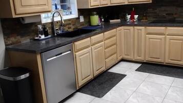 Una cocina con armarios de madera clara, lavavajillas de acero inoxidable y piso de baldosas.