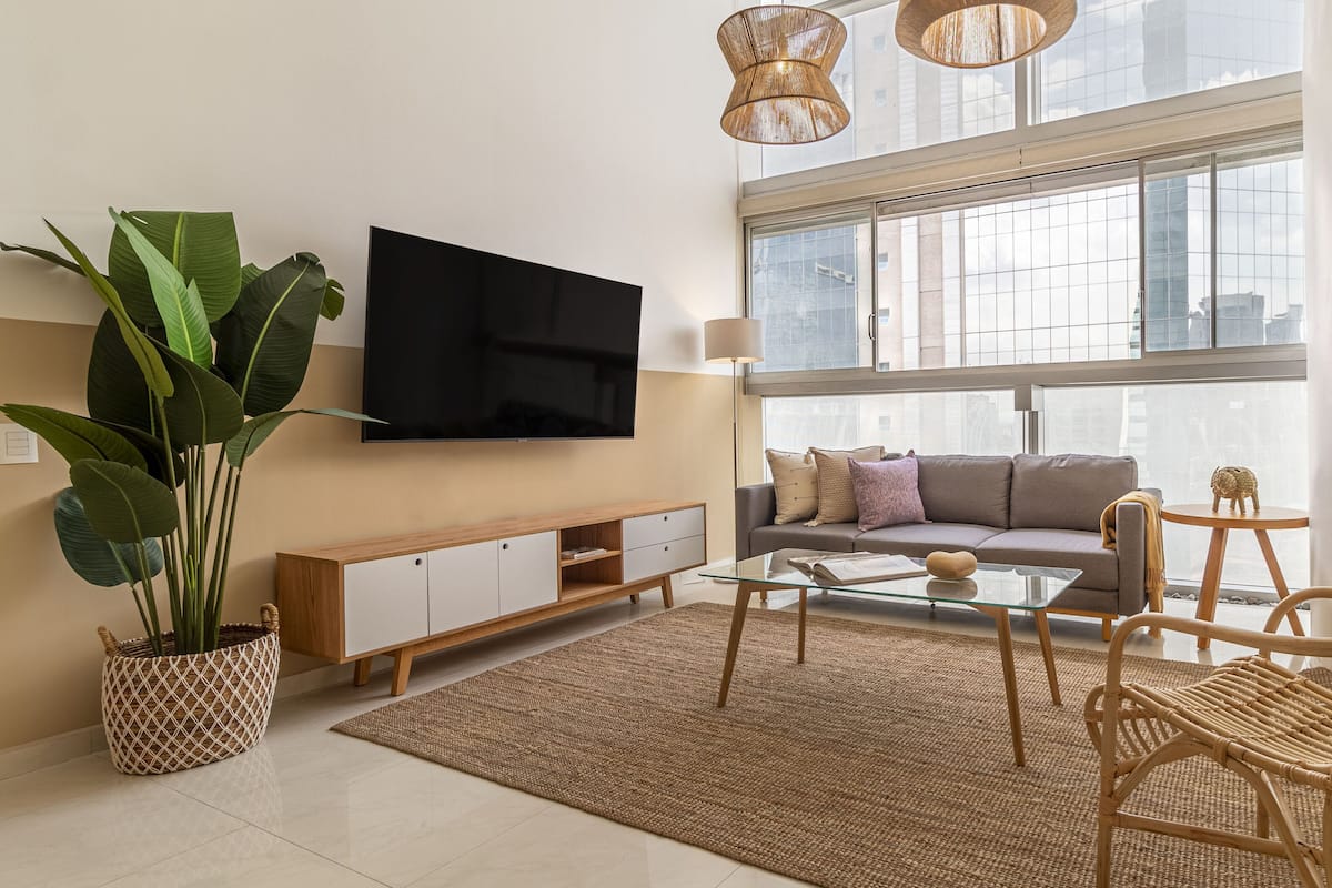 A modern living room with a flat-screen TV, a sofa, a glass coffee table, and a large potted plant.