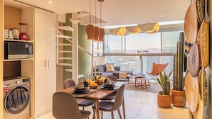 A modern kitchen with a built-in washer and dryer, a dining area with a table and chairs, and a view of the city through large windows.