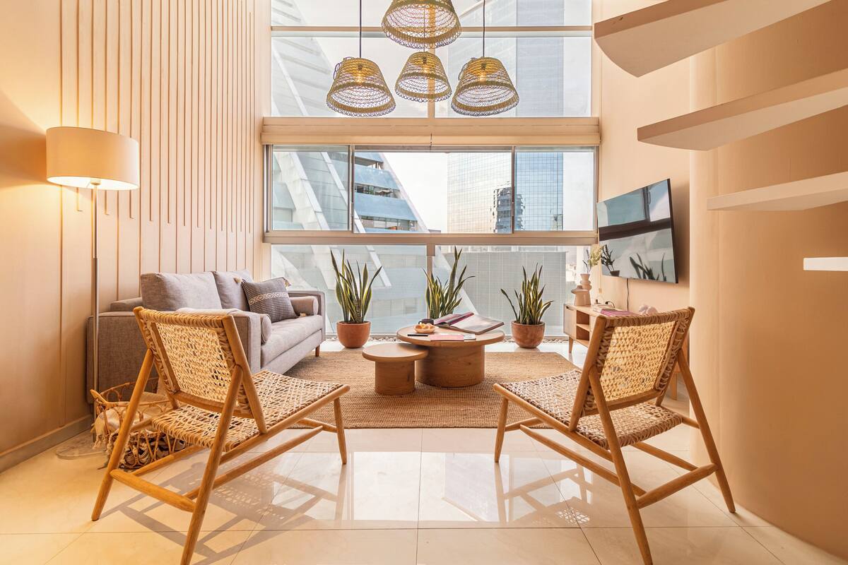 A modern living room with a sofa, two wicker chairs, a coffee table, and potted plants.