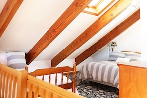 Un dormitorio con techo inclinado, vigas de madera, cama con ropa de cama a rayas, una mesita de noche y una lámpara.