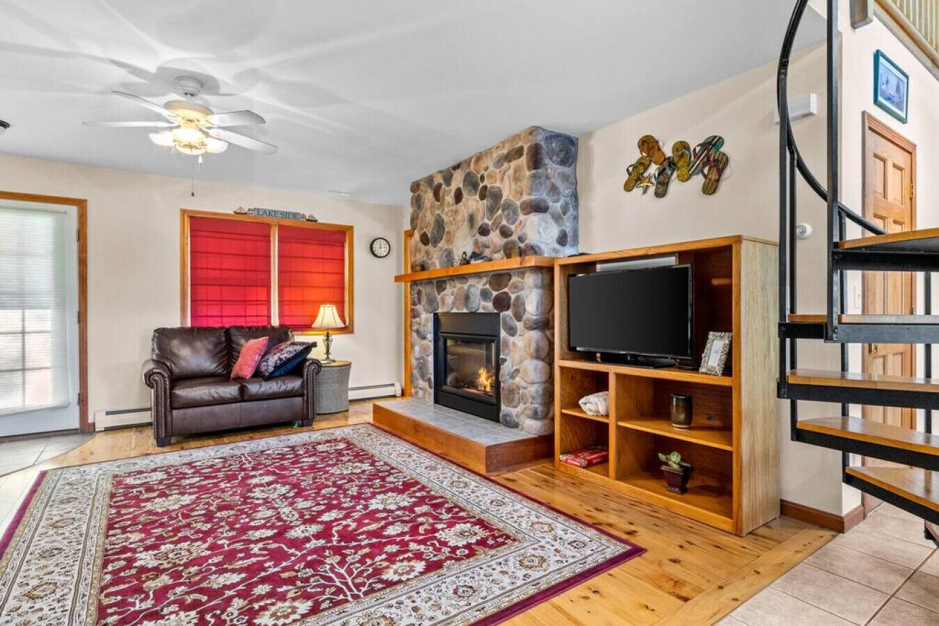 A living room with a stone fireplace, a leather sofa, a red rug, and a TV on a wooden stand.