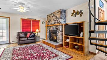 A living room with a stone fireplace, a leather sofa, a red rug, and a TV on a wooden stand.