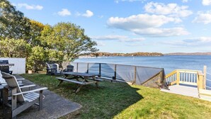 A backyard with a picnic table, chairs, and a grill area overlooking a lake. - Cottage · Beachfront Cottage on Lake Champlain, Colchester (Colchester)