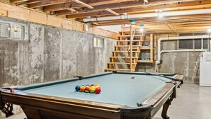 Una mesa de billar con bolas en una habitación con paredes de concreto y vigas de madera.