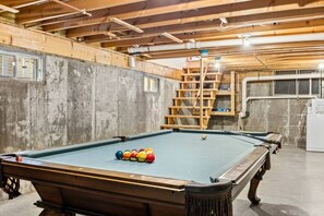 Una mesa de billar con bolas en una habitación con paredes de concreto y vigas de madera.