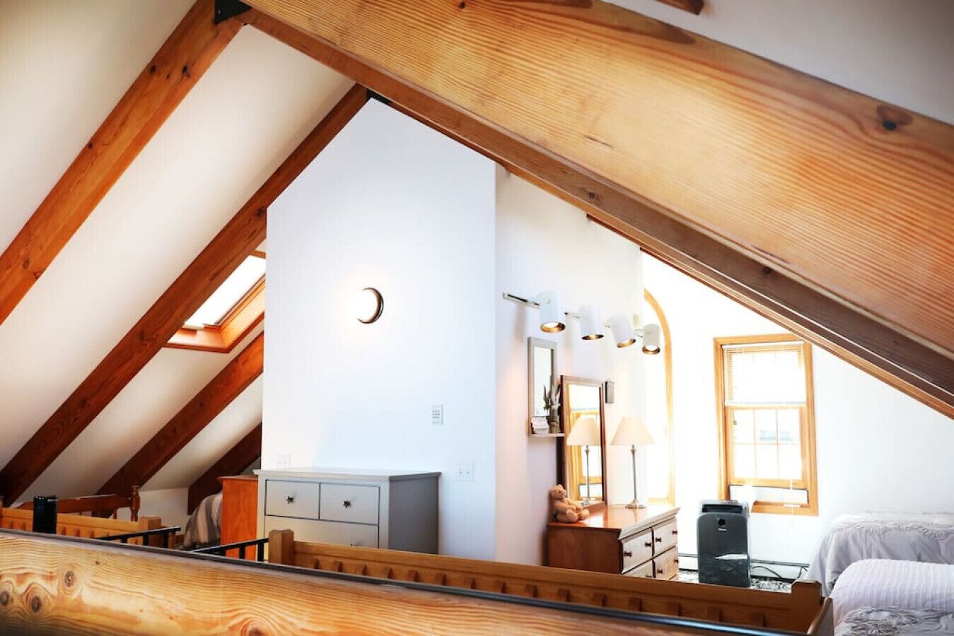 A bedroom with a sloped ceiling, a bed, a dresser, and a desk.