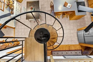 A spiral staircase with a wooden finish and black metal railings, leading to a dining area with wooden tables and chairs. - Cottage · Beachfront Cottage on Lake Champlain, Colchester (Colchester)