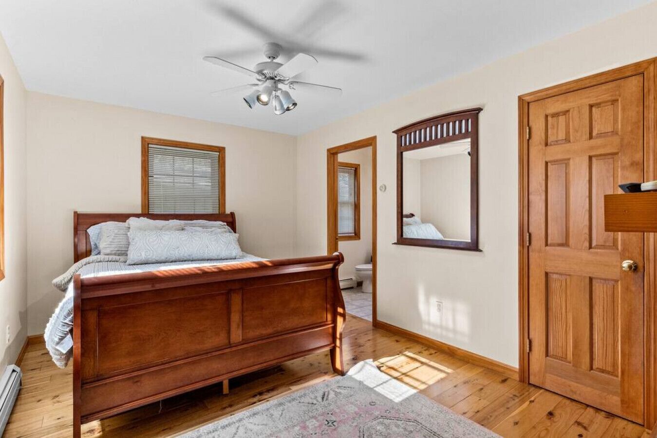 A bedroom with a wooden bed, a ceiling fan, a wooden door, and a window with blinds.