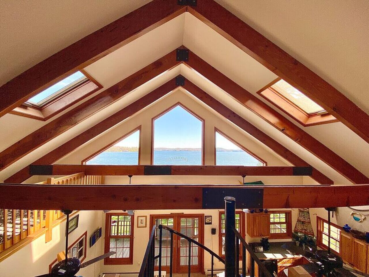 A spacious attic room with skylights, wooden beams, and a view of the water.