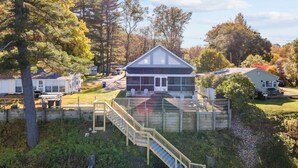 A residential area with a house featuring a covered porch and a staircase leading to a deck. - Cottage · Beachfront Cottage on Lake Champlain, Colchester (Colchester)