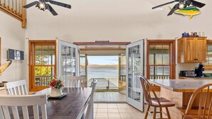 A dining area with a view of the sea, wooden furniture, and ceiling fans. - Cottage · Beachfront Cottage on Lake Champlain, Colchester (Colchester)
