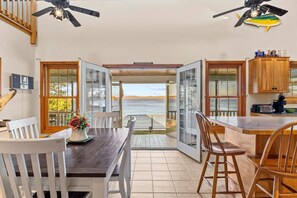 A dining area with a view of the sea, wooden furniture, and ceiling fans. - Cottage · Beachfront Cottage on Lake Champlain, Colchester (Colchester)