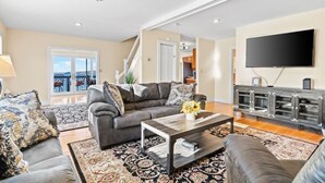A spacious living room with a grey sofa set, a coffee table, and a flat-screen TV mounted on the wall.