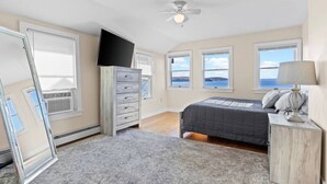 Un dormitorio con cama, cómoda, televisor y ventanas con vistas.