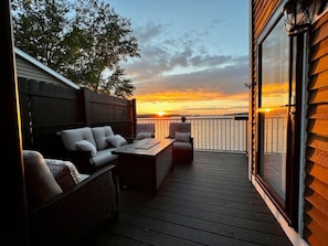Une terrasse avec un canapé et des fauteuils donnant sur un coucher de soleil.
