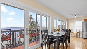 A spacious dining area with a large table and chairs, a view of the ocean through sliding glass doors, and a kitchen area with a refrigerator.