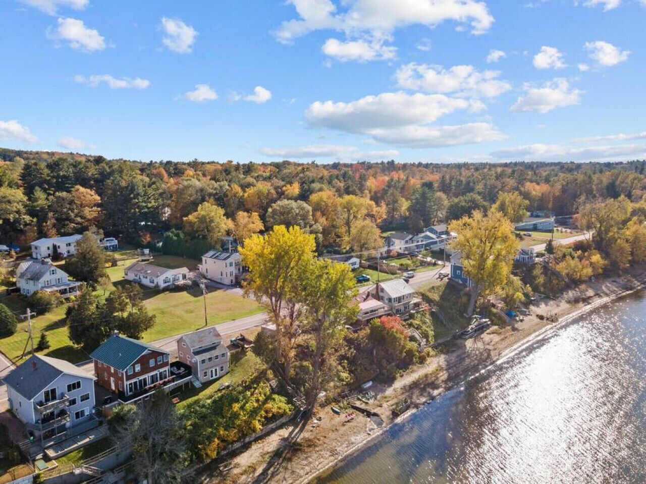 Ett flygbildsbild av ett bostadsområde med hus längs en flod, omgivet av höstlövsverk.