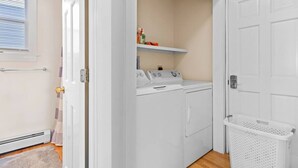 A laundry room with a washer and dryer, a basket, and a shelf with cleaning supplies.