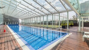 An indoor swimming pool with clear glass walls, a wooden deck, and a view of the city skyline. - Casa Reforma by Kukun  (Mexico City)