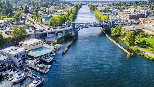 A river with a bridge, boats docked on the riverbank, and buildings along the river.