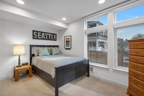 Um quarto com cama, cômoda, mesa de cabeceira, abajur, quadro e janela com persianas.