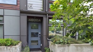 A modern building entrance with a grey door marked '4800A' and concrete planters with greenery.
