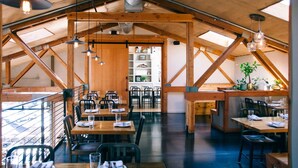 A restaurant with wooden beams, tables, chairs, and hanging pendant lights.