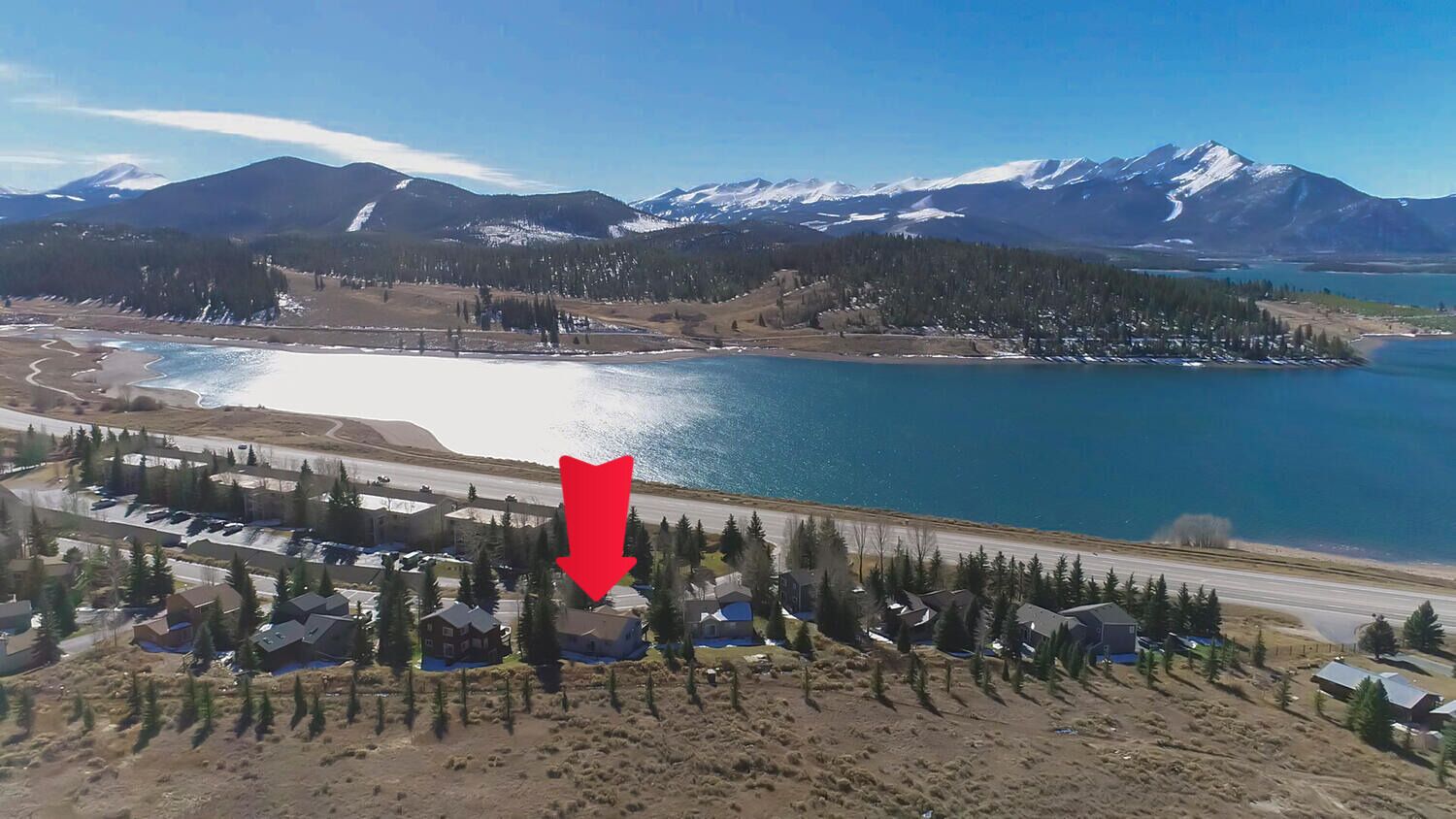 Área residencial com casas, uma estrada e um lago com montanhas ao fundo.