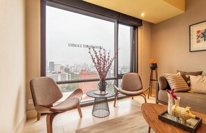 Un salon moderne avec une grande fenêtre, deux fauteuils, une petite table ronde, un canapé et un vase décoratif.