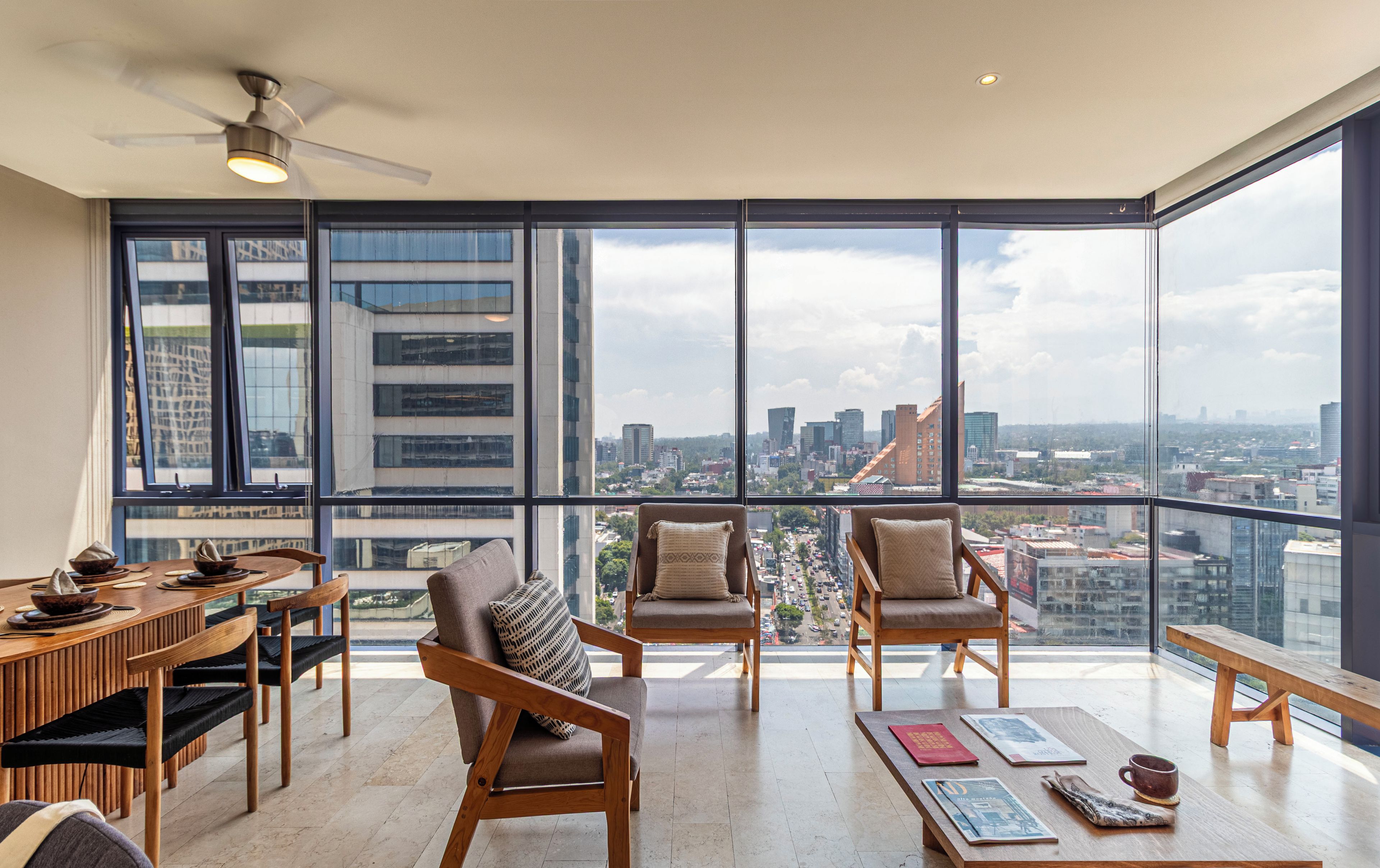 Un balcón amplio con vista a la ciudad, mobiliario de madera y un ventilador de techo.