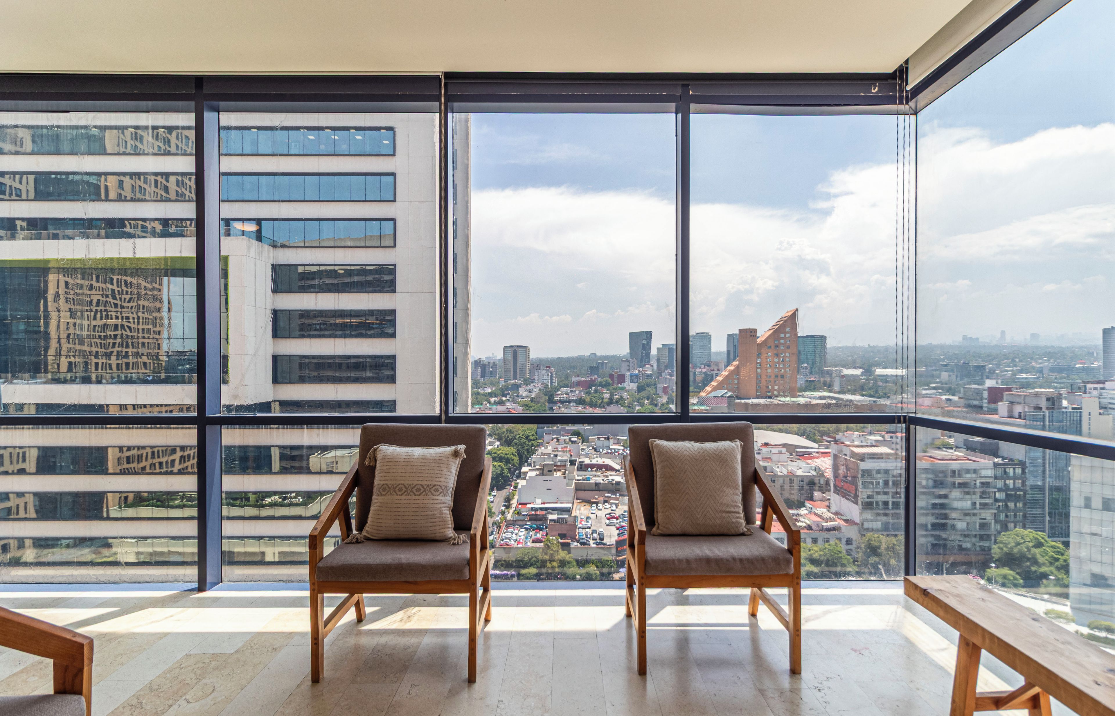 Un apartamento alto con un balcón grande, dos sillas de madera y vista a un paisaje urbano.
